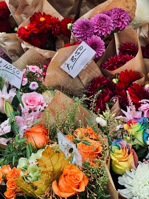A vibrant assortment of freshly arranged flower bouquets featuring a variety of blooms such as red dahlias, purple chrysanthemums, pink roses, orange roses, and multicolored spray roses. The flowers a